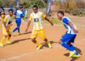 Young soccer players in yellow and blue uniforms competing on a sandy field, with spectators and a 10bet.co.za banner in the background.