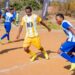 Young soccer players in yellow and blue uniforms competing on a sandy field, with spectators and a 10bet.co.za banner in the background.